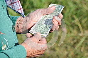 The old woman is holding money in her hands. An elderly woman with dollars in her hands. Poverty alms