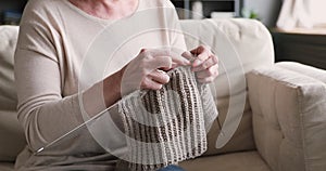 Old woman holding needles knitting scarf on sofa, closeup view