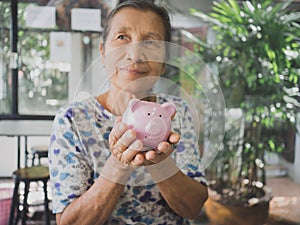 Old woman holding Pink piggy bank with two hands. Saving money for future plan and retirement fund concept