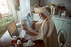 Old woman holding x-ray and having online consultation with doctor