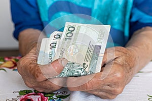 An old woman holds 100 Polish zloty banknotes in her hands, Polish money, Pensioners finance concept