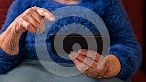 Old woman at home using a mobile phone. Hands of grandmother holds a smartphone