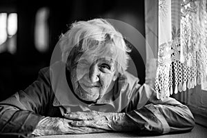 An old woman in the house sitting at the table. Black and white photoÑŽ