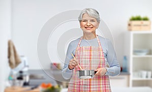old woman in kitchen apron with pot cooking food
