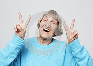 Old woman laugh and showing peace or victory signat camera. Emotion and feelings. Portrait of expressive grandmother.