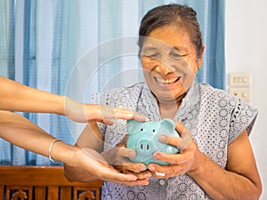 Old woman looking scared trying to protect her blue piggy bank from Financial fraud, Saving money for future plan and retirement