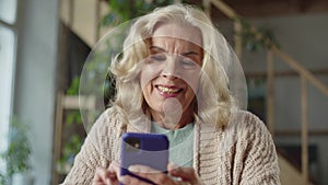 An old woman looks at photographs on the phone. She likes them from what she laughs