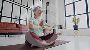 Old woman make yoga exercise at home. Mature woman have meditation. Put hands together and smile. Start the day with