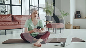 Old woman make yoga exercise at home. Mature woman Use mobile phone for online browsing or internet purchases. Woman use