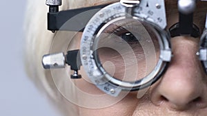 Old woman in optical trial frame sitting in eye doctor cabinet, vision checkup