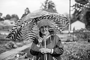 An old woman outdoors standing under a umbrella. Black and white photo.