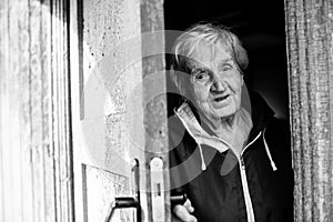 An old woman peeks out from behind the door of his house. Black and white photo.