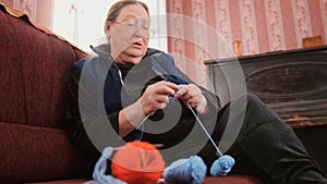 Old woman pensioner home - knits wool socks sitting on the sofa - elderly lady hobby