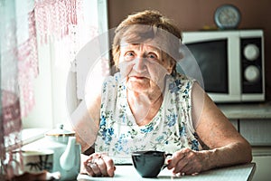 An old woman pensioner sits at a table in her home. Portrait.