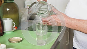 An Old Woman Pours Water From A Decanter Into A Glass