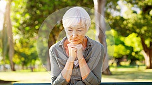 Old woman, praying or thinking in park, sad with grief or loss, dementia diagnosis and health scare with faith or
