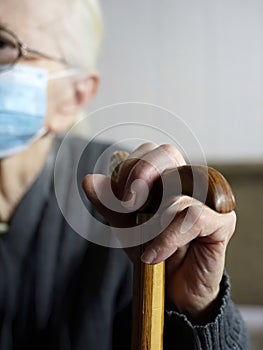 An old woman with a protective face mask holds a stick handle indoors  quarantine