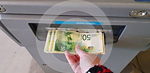 Old woman pulls banknotes Israeli shekels from atm