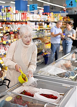 Old woman purchaser choosing frozen pepper in supermarket