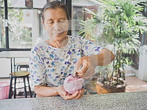 Old woman putting coin into Pink piggy bank. Saving money for future plan and retirement fund concept