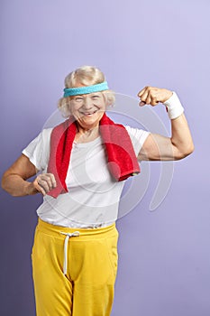 Old woman raising one hand, showing strength of her musculs, sport achievement.