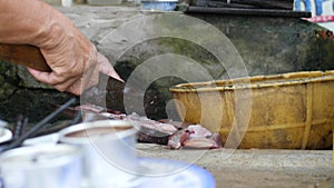 Old woman`s hand slicing fish on a wooden board in Asian dirty kitchen.