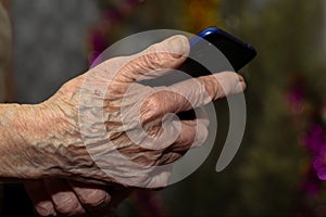 Old woman& x27;s wrinkled hand holding modern mobile phone