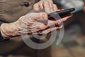 Old woman& x27;s wrinkled hands hold a modern mobile phone