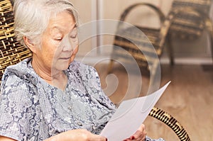 Old woman seated reading carefully a document or terms of a insurance. Old obaasan (grandma), japanese descendant. photo