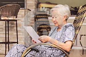 Old woman seated reading carefully a document or terms of a insurance. Old obaasan (grandma), japanese descendant. photo
