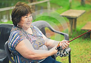 Old woman seated, smiling, fishing, holding a fishing rod. B