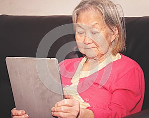 Old woman seated on a sofa using a touchscreen tablet photo