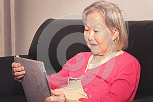 Old woman seated on a sofa using a touchscreen tablet photo