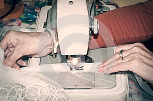 Old woman sewing wedding dress on vintage sewing machine.