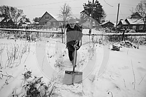 An old woman is shoveling snow outside her village home. Black and white photo.
