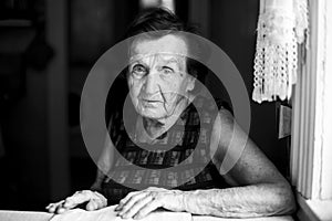 An old woman sits in her house. Black and white photo.