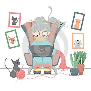 Old woman sitting in an armchair with laptop and her cats at home.
