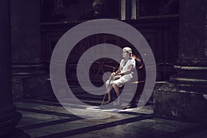 Old woman sitting in colored light on church bench