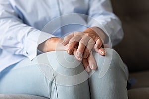 Old woman sitting on couch folded hands on knees closeup