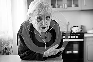 An old woman sitting in the kitchen by the window in his house.