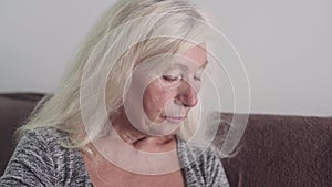 Old woman sitting and looking at the side at home room, sad grandmother portrait on the white color background. Lonely