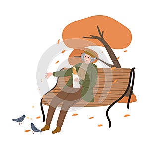 Old woman sitting in park with fresh bread and feeding pigeons in autumn city