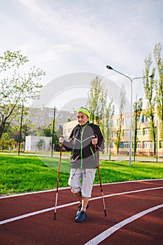 Old woman in sportswear practicing nordic walking outdoors on rubber treadmill in stadium. Older female walk by scandinavian walk