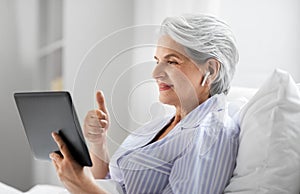 old woman with tablet pc having video call in bed
