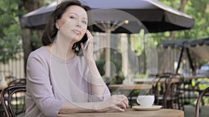 Old Woman Talking on Phone, Sitting in Outdoor Cafe