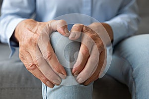 Old woman touching knee feeling pain suffering from osteoarthritis, closeup