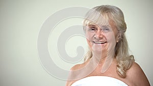 Old woman in towel smiling on camera, happy client before beauty procedures