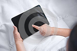 Old woman using tablet and sitting on white sofa