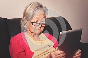 Old woman wearing glasses at home reading something tablet photo