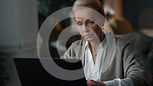 Old woman working laptop computer at home. Elderly lady looking laptop